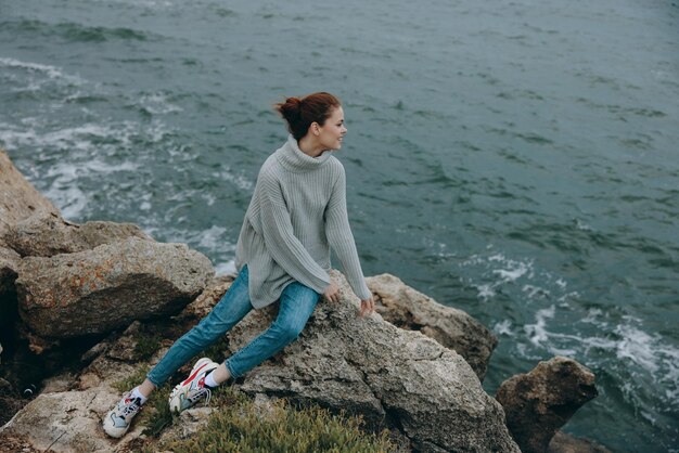 Portret van een vrouw in een grijze trui staat op een rotsachtige kust natuur Ontspanningsconcept