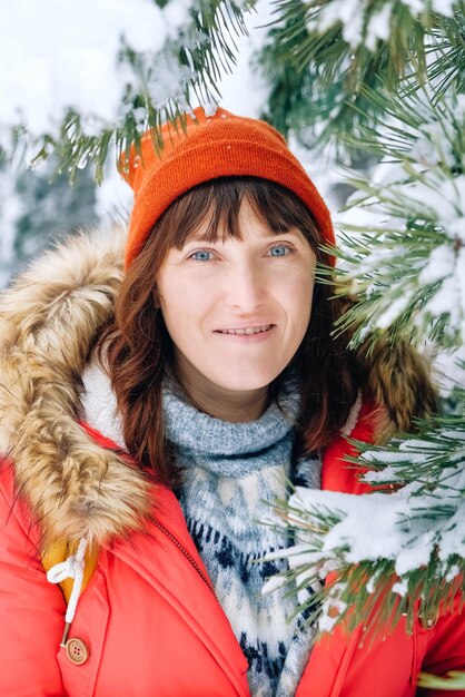 Portret van een vrouw in een rode warme jas en muts in een besneeuwd winterbos