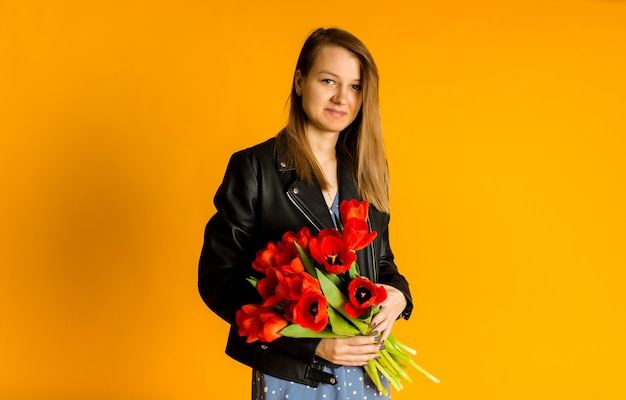 Portret van een vrouw in een zwart leren jasje met een boeket rode tulpen op een gele achtergrond met ruimte voor tekst