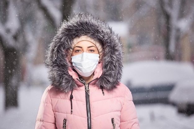 Portret van een vrouw in roze die in de winter door de straat loopt onder sneeuwval in een beschermend masker ter bescherming tegen infectieziekten Bescherming tegen verkoudheid griep luchtvervuiling Gezondheidsconcept