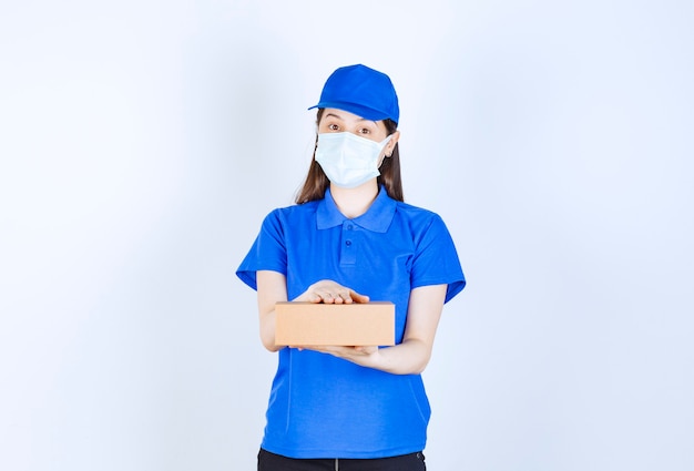 Portret van een vrouw in uniform en medisch masker met papieren doos