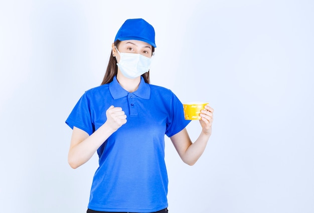 Portret van een vrouw in uniform en medisch masker met plastic beker