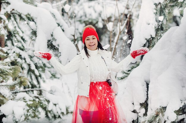 Portret van een vrouw in witte kleren en een rode hoed in een koud winterbos. Meisje in een besneeuwd winterbos