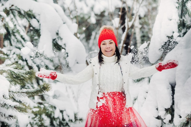 Portret van een vrouw in witte kleren en een rode hoed in een koud winterbos. Meisje in een besneeuwd winterbos