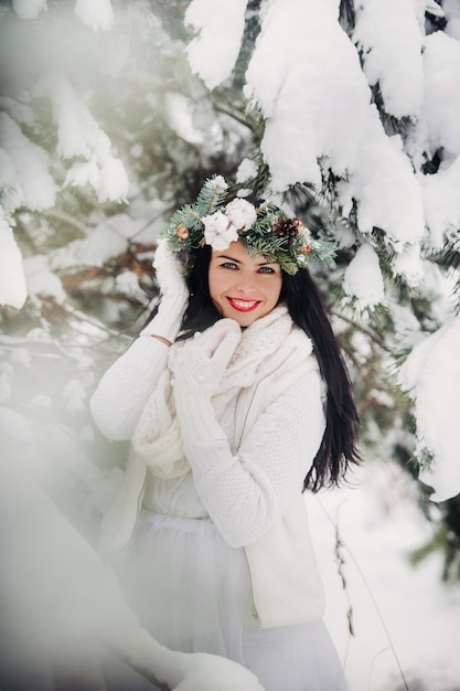 Portret van een vrouw in witte kleren in een koude winterbos. Meisje met een krans op haar hoofd in een met sneeuw bedekte winterbos.