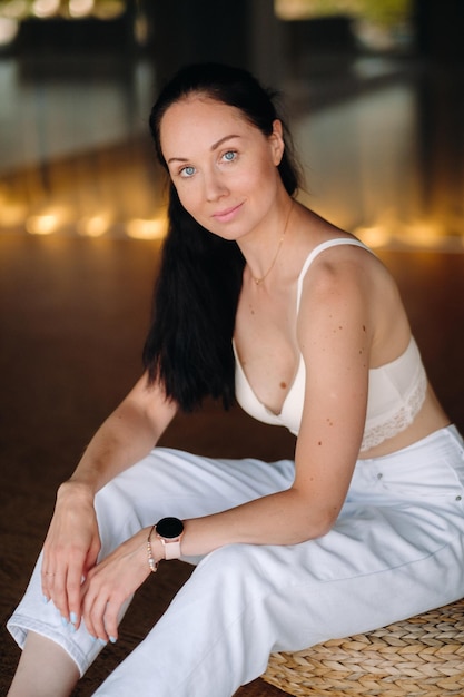 Portret van een vrouw in witte kleren zittend op een poef in het interieur