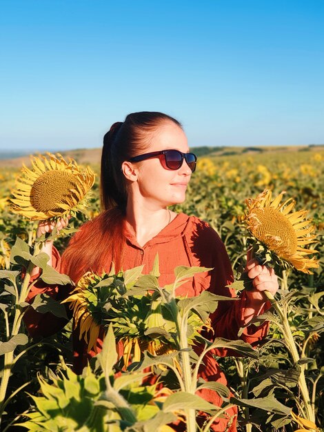 Portret van een vrouw in zonnebril in een veld met zonnebloemen