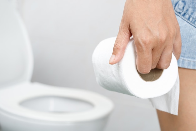 Portret van een vrouw lijdt aan diarree zijn maag pijnlijk. pijn en probleem. hand houden tissuepapier rol voor toiletpot. constipatie in de badkamer. hygiëne, gezondheidszorgconcept.