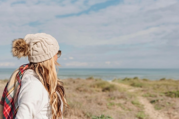 Portret van een vrouw met bobbelhoed op het strand kijkend naar de zee