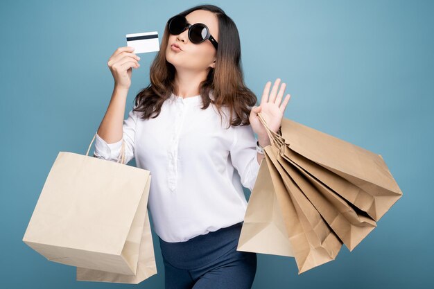 Foto portret van een vrouw met boodschappenzakken en een creditcard terwijl ze tegen een blauwe achtergrond staat