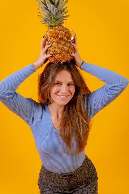 Portret van een vrouw met een ananas in een zonnebril in een studio op een gele achtergrond gezonde zomer