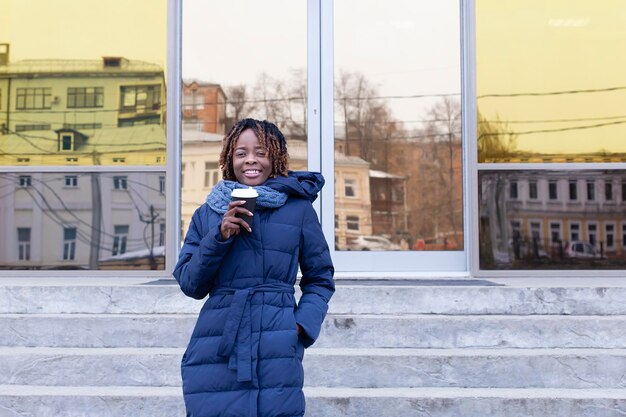 Portret van een vrouw met een koffiekop bij de ingang van het gebouw