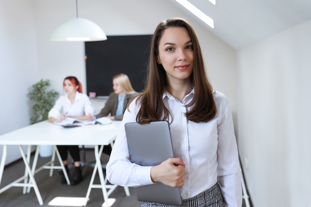 Portret van een vrouw met een laptop op de achtergrond van een werkend kantoor