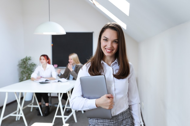 Portret van een vrouw met een laptop op de achtergrond van een werkend kantoor