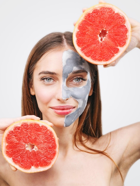 Portret van een vrouw met een masker met een vers schijfje grapefruit in haar handen geïsoleerd op een witte achtergrond