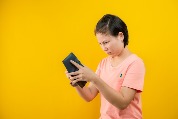 Portret van een vrouw met een portemonnee die spijt heeft dat er geen geld in haar tas zit tegen een gele achtergrond.