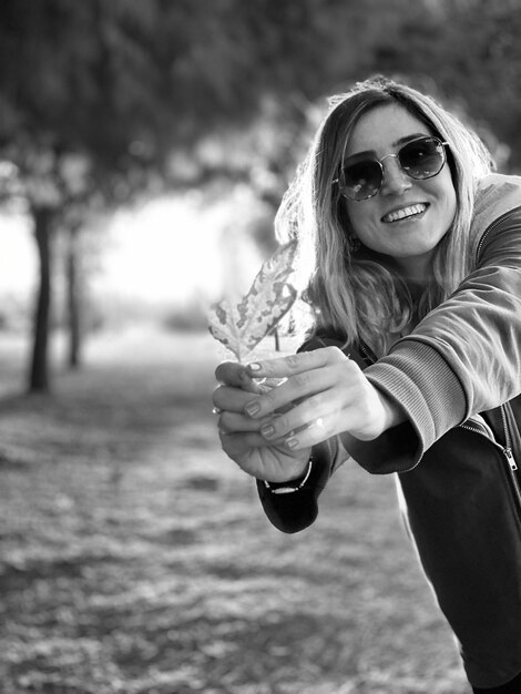 Foto portret van een vrouw met een zonnebril die een blad vasthoudt in het park