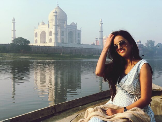 Foto portret van een vrouw met een zonnebril die tegenover de taj mahal zit