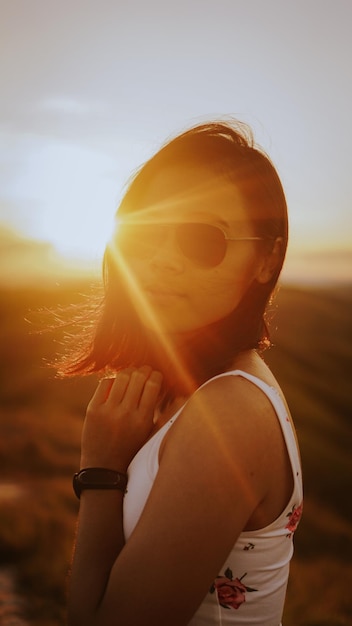 Portret van een vrouw met een zonnebril terwijl ze tijdens de zonsondergang op het land tegen de hemel staat