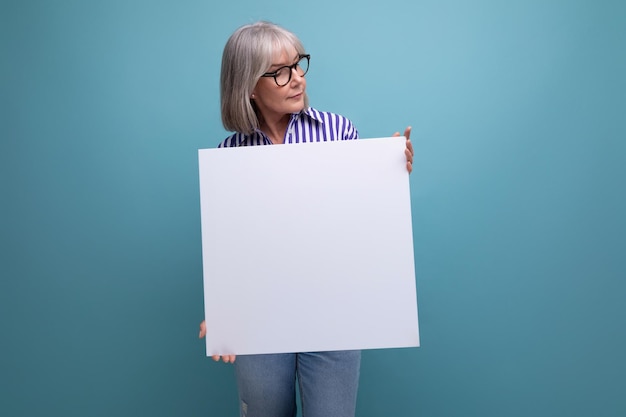 Portret van een vrouw met grijs haar die een leeg vel met een mockup op een heldere studioachtergrond laat zien