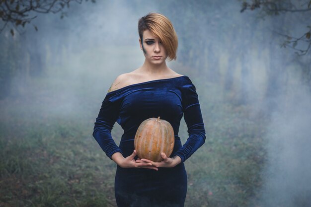 Portret van een vrouw met pompoen tussen de bomen in de mist