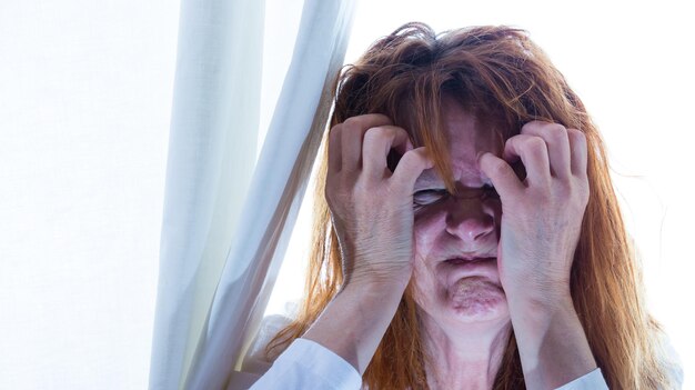 Foto portret van een vrouw met verwikkelde haren ze staat achter een gordijn en is ongelukkig