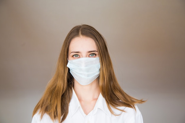 Portret van een vrouw op beige, die een medisch masker draagt. Demonstratie van medische apparatuur.