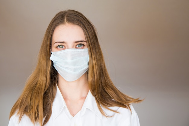 Portret van een vrouw op een beige achtergrond, die een medisch masker draagt