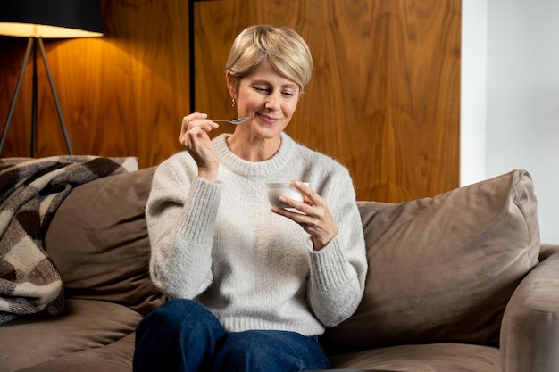 Portret van een vrouw van middelbare leeftijd die thuis op de bank yoghurt eet