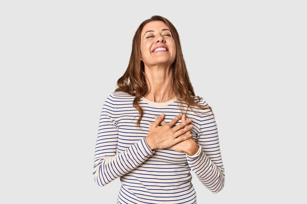 Portret van een vrouw van middelbare leeftijd in een studio, lachend, handen op het hart, concept van geluk