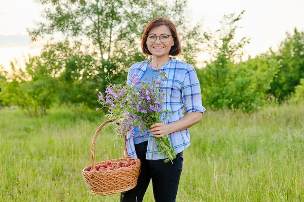 Portret van een vrouw van middelbare leeftijd met een boeket wilde bloemen en een mandje aardbeien in de natuur