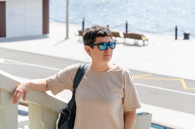 Portret van een vrouw van middelbare leeftijd met zwart kort haar en een zonnebril Een vrouw kijkt in de verte tegen de achtergrond van de stadsdam op een zonnige zomerdag