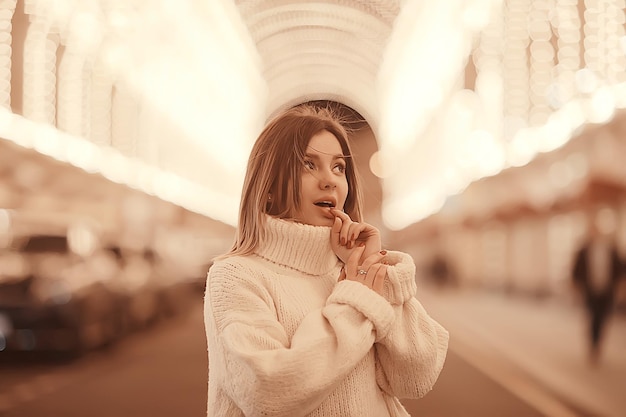 portret van een vrouw witte trui winter, seizoensgebonden buiten stadswandeling in de avondstad