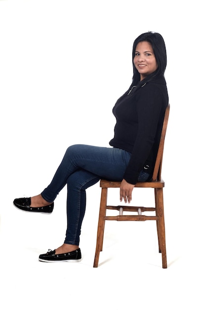 portret van een vrouw zittend op een stoel op een witte achtergrond, benen gekruist en camera kijken