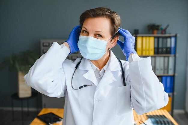 Portret van een vrouwelijke arts die een gezichtsmasker draagt en haar patiëntenkaart op een digitale tablet houdt terwijl ze in het ziekenhuis staat