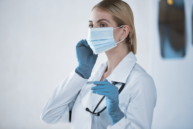 Portret van een vrouwelijke arts in een witte jas, medisch masker en handschoenen