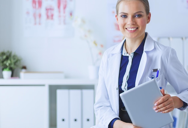 Portret van een vrouwelijke arts in een ziekenhuisgang die een tabletcomputer vasthoudt en glimlachend naar de camera kijkt
