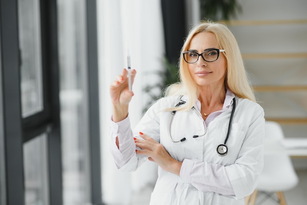 Portret van een vrouwelijke arts van middelbare leeftijd draagt een witte doktersjas met een stethoscoop om haar nek Glimlachende arts die zich in een privékliniek bevindt