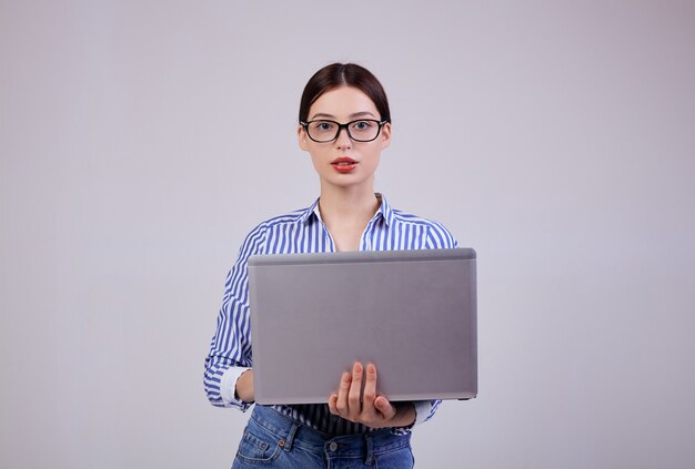 Portret van een vrouwelijke beheerder in een gestreept wit-blauw shirt met een bril en een laptop op grijs. Werknemer van het jaar.
