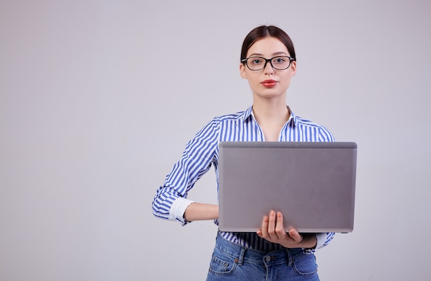 Portret van een vrouwelijke beheerder in een gestreept wit-blauw shirt met een bril en een laptop op grijs.