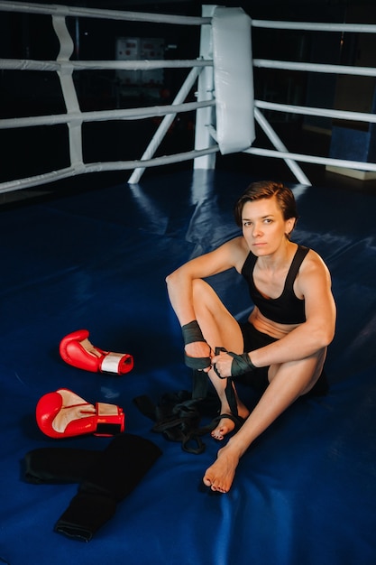 Portret van een vrouwelijke bokser met rode handschoenen na training zittend in de ring.