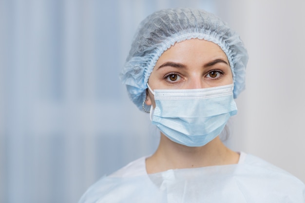 Portret van een vrouwelijke dokter, in een beschermend blauw pak, en een medisch masker op haar gezicht