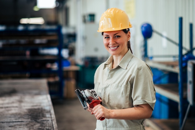 Portret van een vrouwelijke fabrieksarbeider met molen op het werk, glimlachend in de camera.