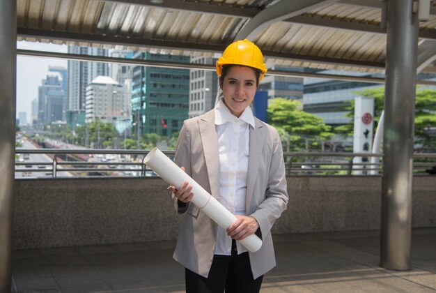 Portret van een vrouwelijke ingenieur met een blauwdruk die in de stad staat