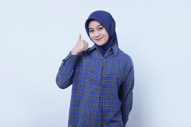 Portret van een vrouwelijke klant die steunt om gelukkig en gelukkig te zijn met het dragen van een hijab met duimen omhoog op een witte muur