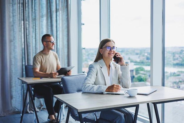 Portret van een vrouwelijke manager in formele kleding die kantoorwerk doet en aan de telefoon praat een succesvolle Europese vrouwelijke baas in optische bril voor oogcorrectie poseren aan haar bureau