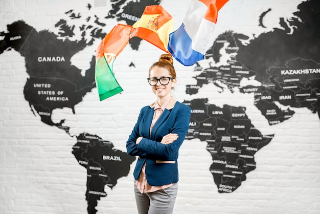 Portret van een vrouwelijke reisagent gekleed in het pak dat binnenshuis staat omringd door vliegende vlaggen op de achtergrond van de wereldkaart