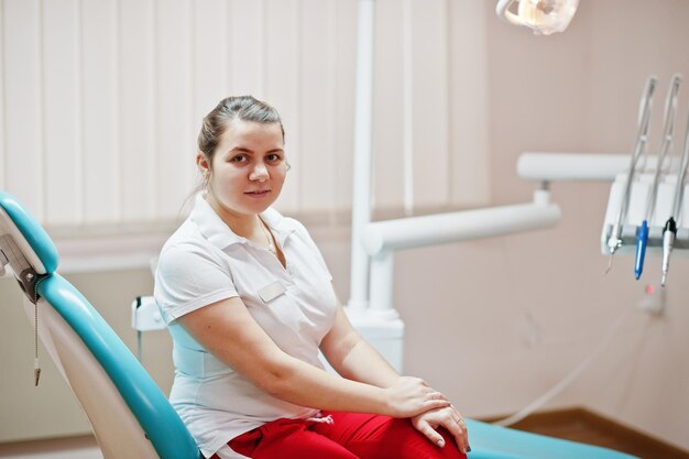 Portret van een vrouwelijke tandartsvrouw die in haar tandheelkundig kantoor op een stoel staat