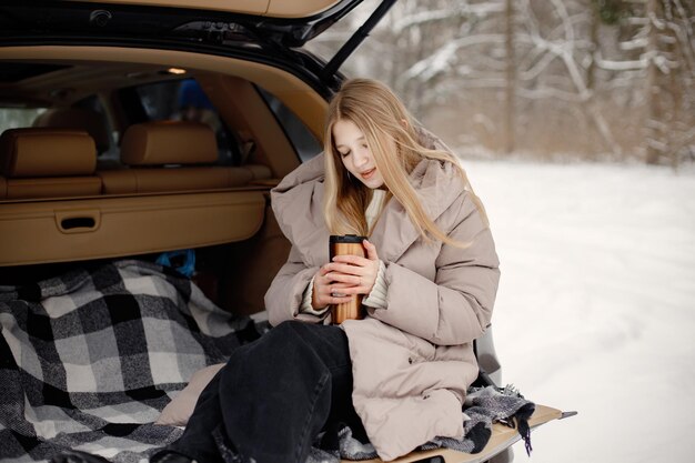 Portret van een vrouwelijke tiener die in de kofferbak van een open auto zit in het winterbos