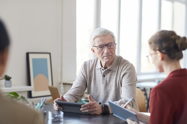 Portret van een witharige senior zakenman die luistert naar een vrouwelijke collega tijdens een briefingvergadering op kantoor